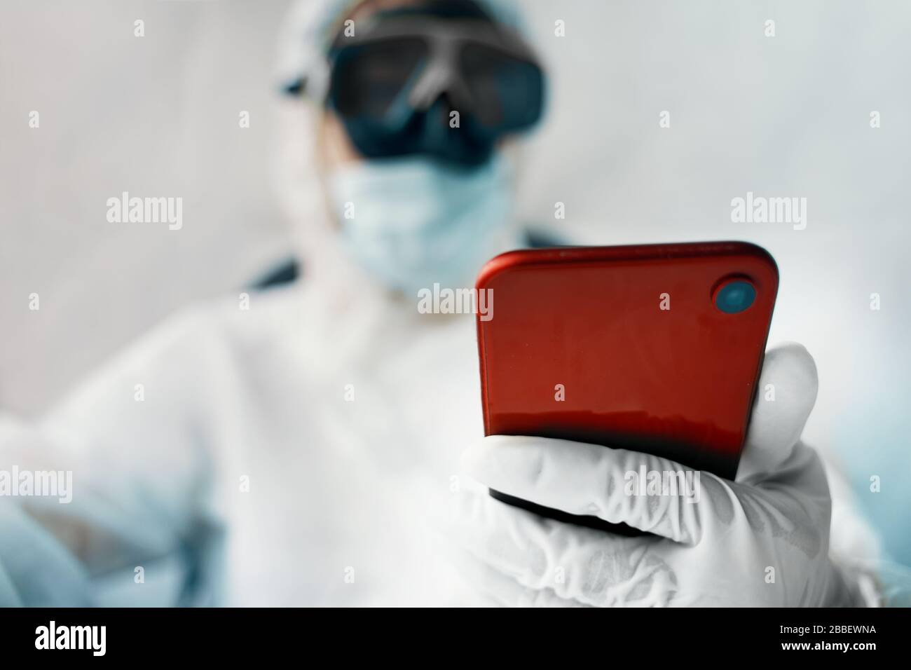 Virologist person protects himself from a global pandemic and holds a phone in his hands. Stock Photo