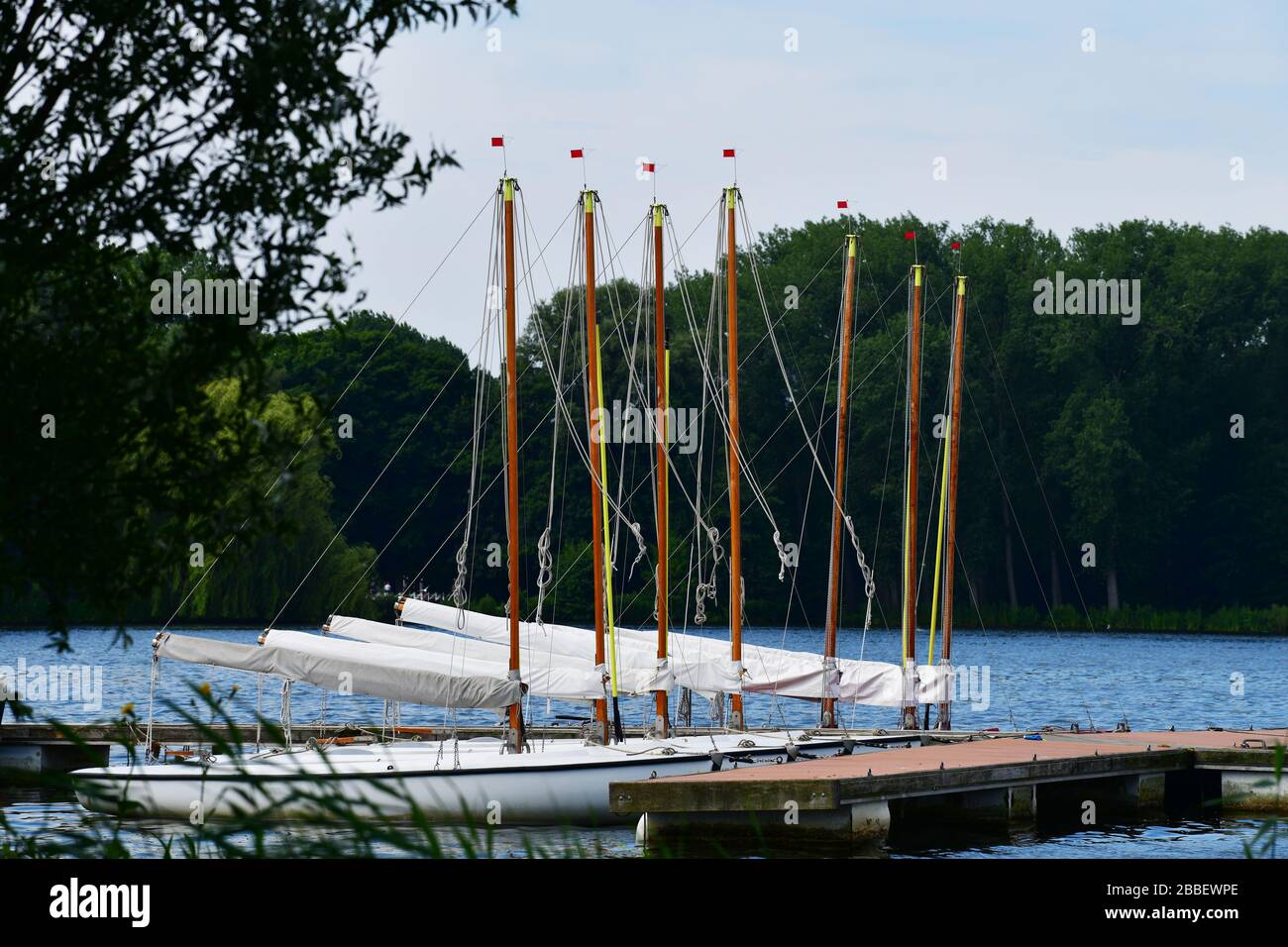 Seven identical sail boats lined up, sails down, at the dock in the Kralingse Plas in Rotterdam Stock Photo
