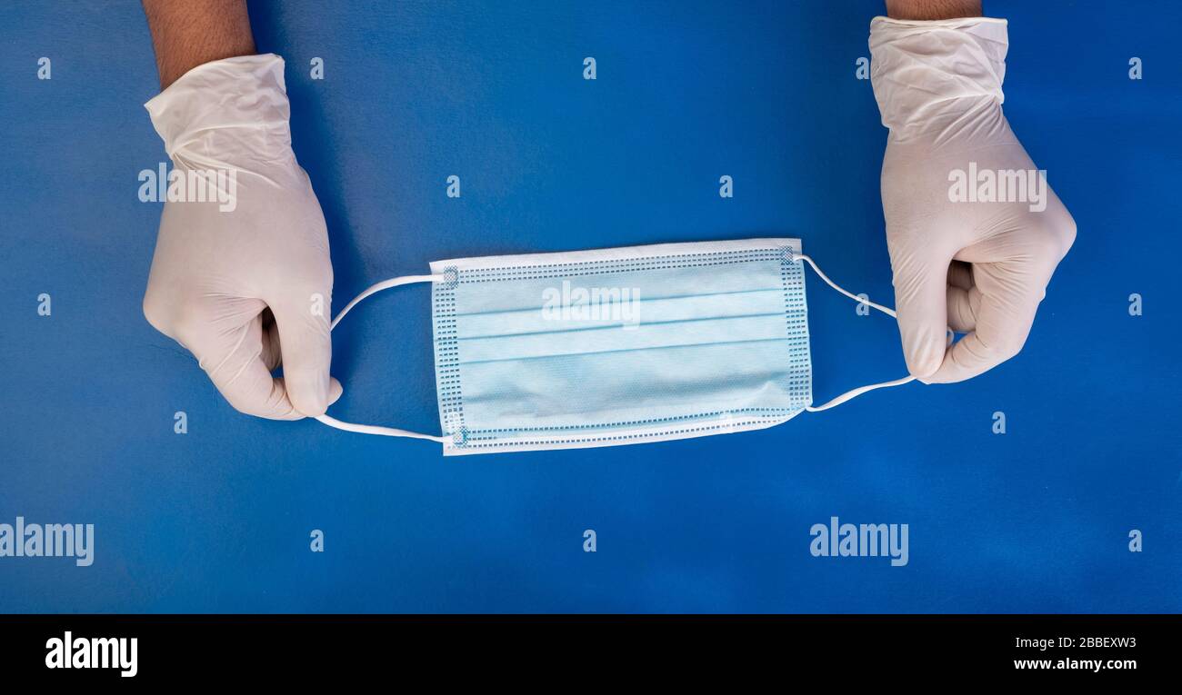 Hands in the blue medical gloves hold a protective medical mask on the ...