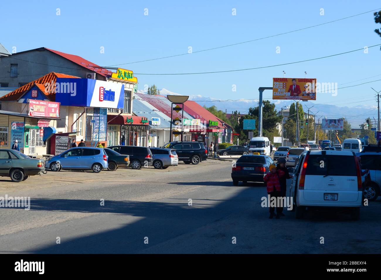 Busy street with multiple cars and commerce in the kyrgyz small town of Karakol in Issyk Kul Region in Kyrgyzstan. Previously Przhevalsk city. Stock Photo