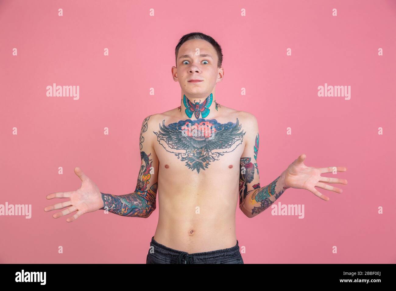 Uncertain. Portrait of young man with freaky appearance on pink background. Unusual look with huge tattooes. Doing daily routine. Human emotions, facial expression, sales, ad concept. Youth culture. Stock Photo