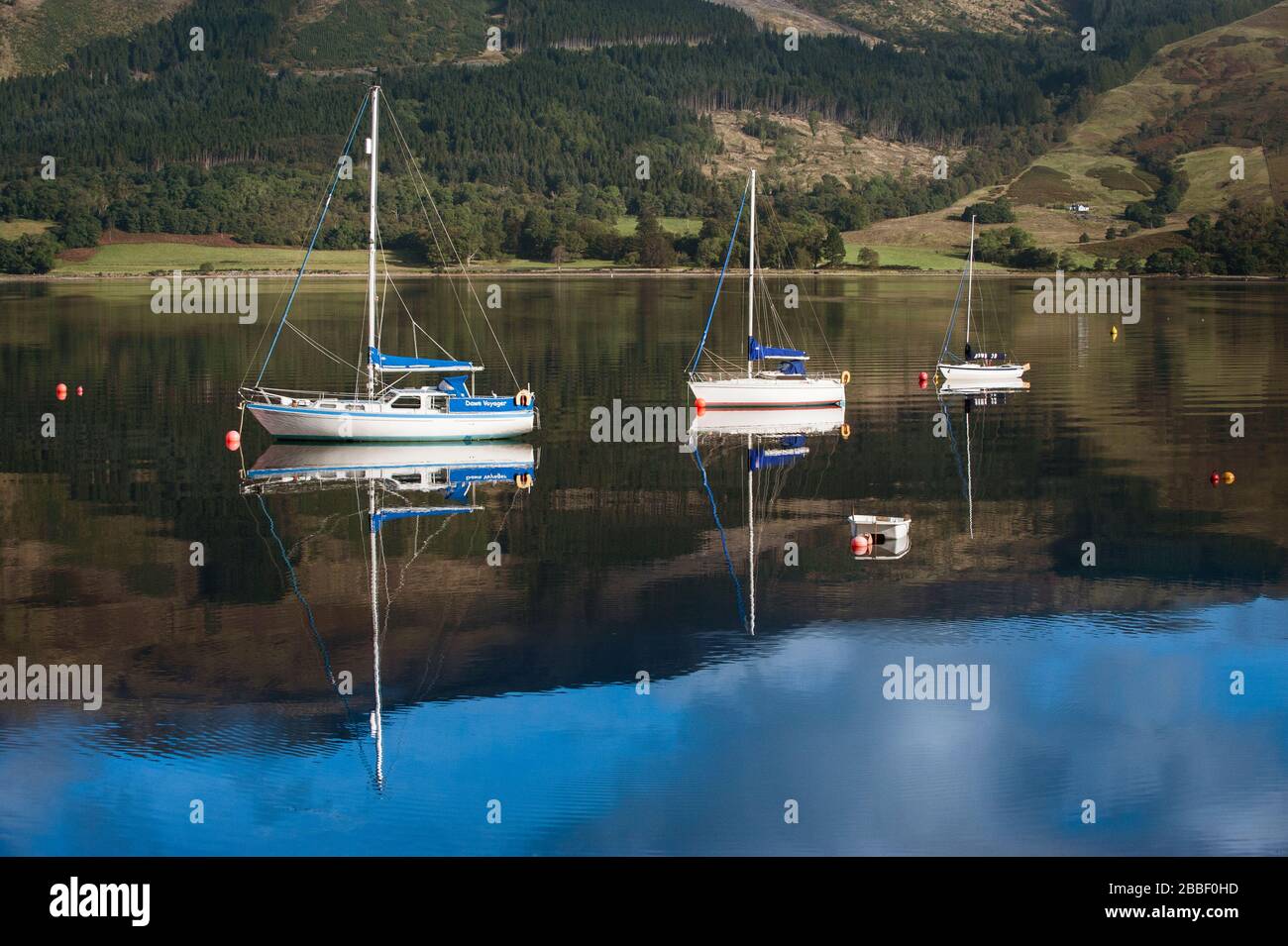 Boats at moorings reflected in the calm tranquil water of Loch Leven in the North West Highlands of Scotland. Stock Photo