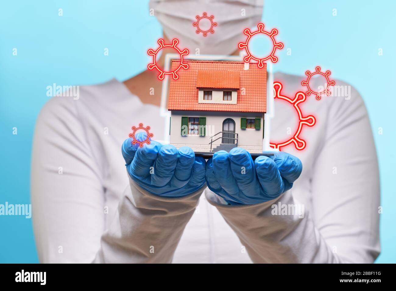 Woman in medical gloves and mask holds house in hands. Concept of home stay, quarantine, security inside the house. Covid-19 Corona Prevention Measure Stock Photo