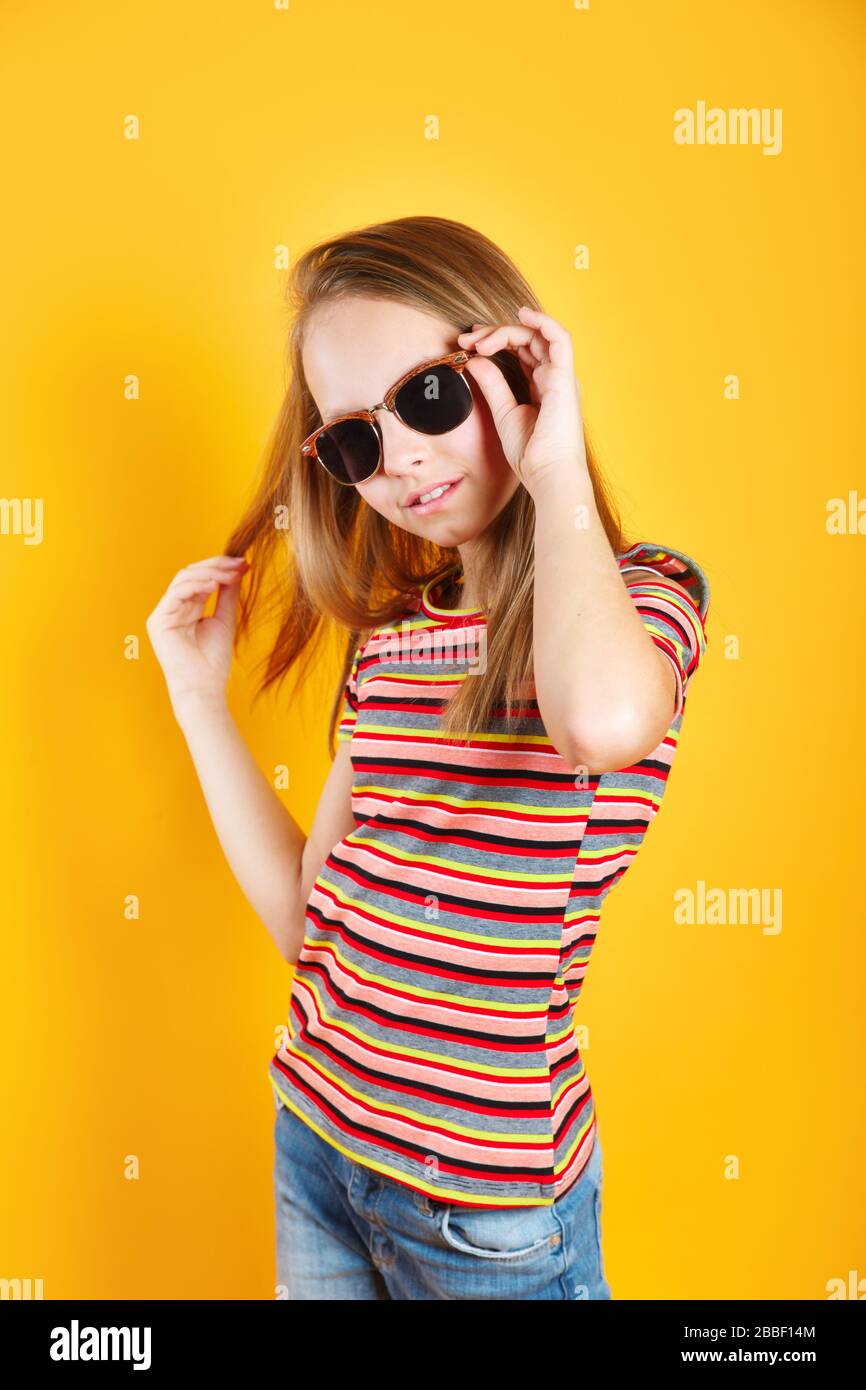 Little girl wearing sunglasses smiling and posing on yellow background Stock Photo