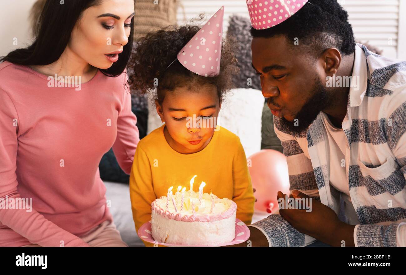 Childs birthday International parents help blow out candles Stock Photo