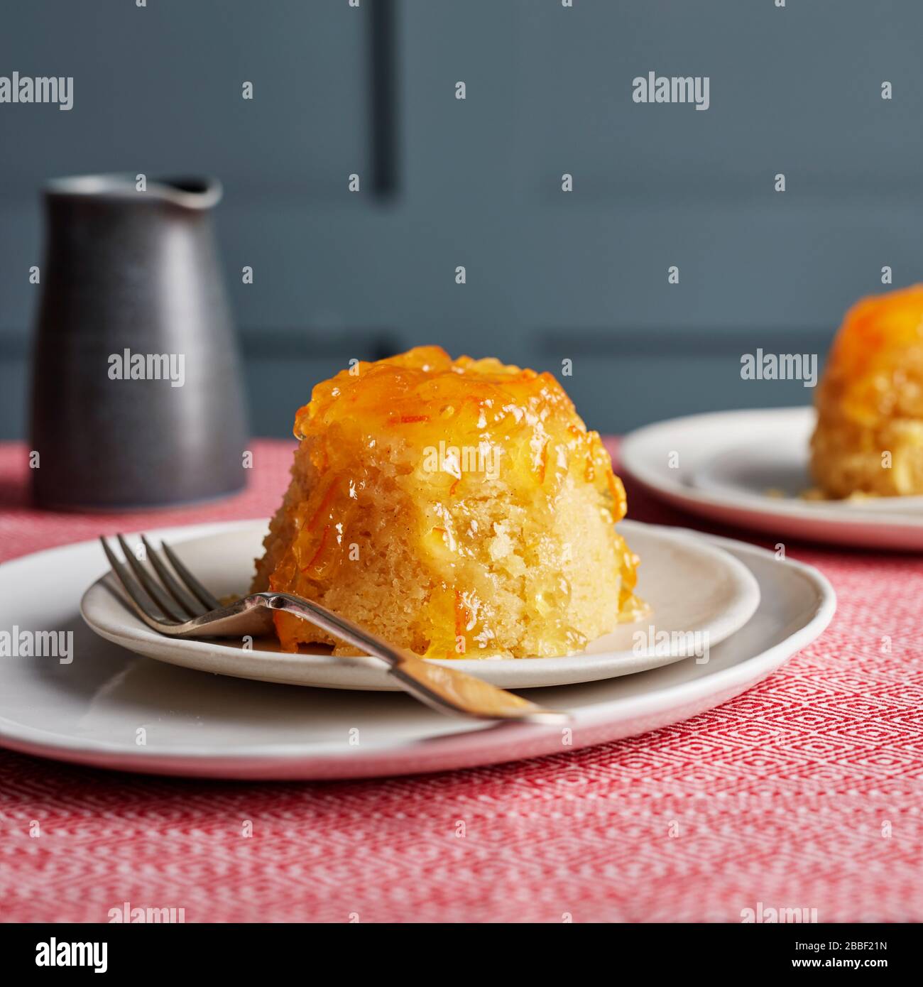 Individual steam sponge puddings marmalade syrup red table top white plates fork gooey sticky dark panelling Stock Photo