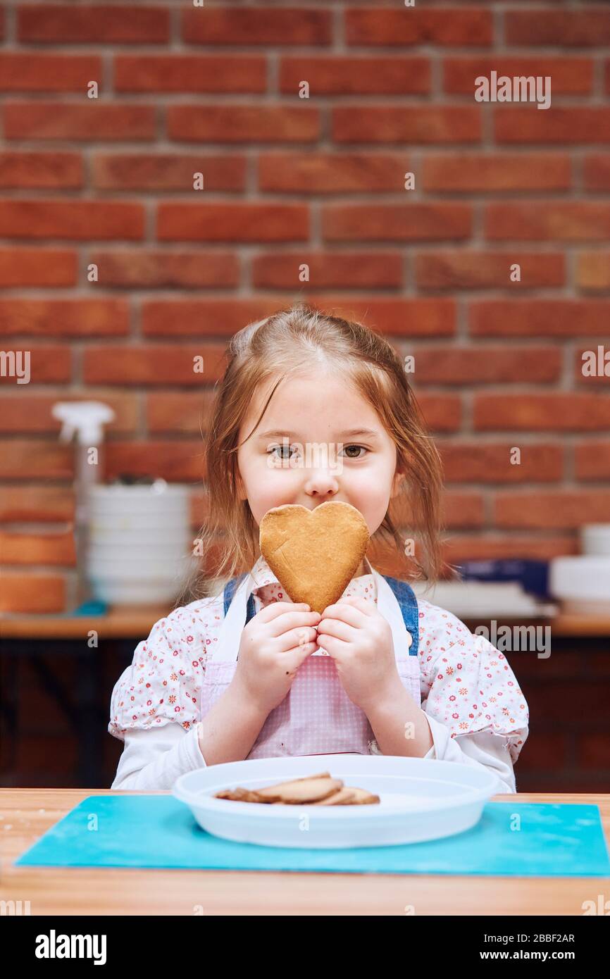 Little girl getting happy out of baked cookie made oneself. Kid taking