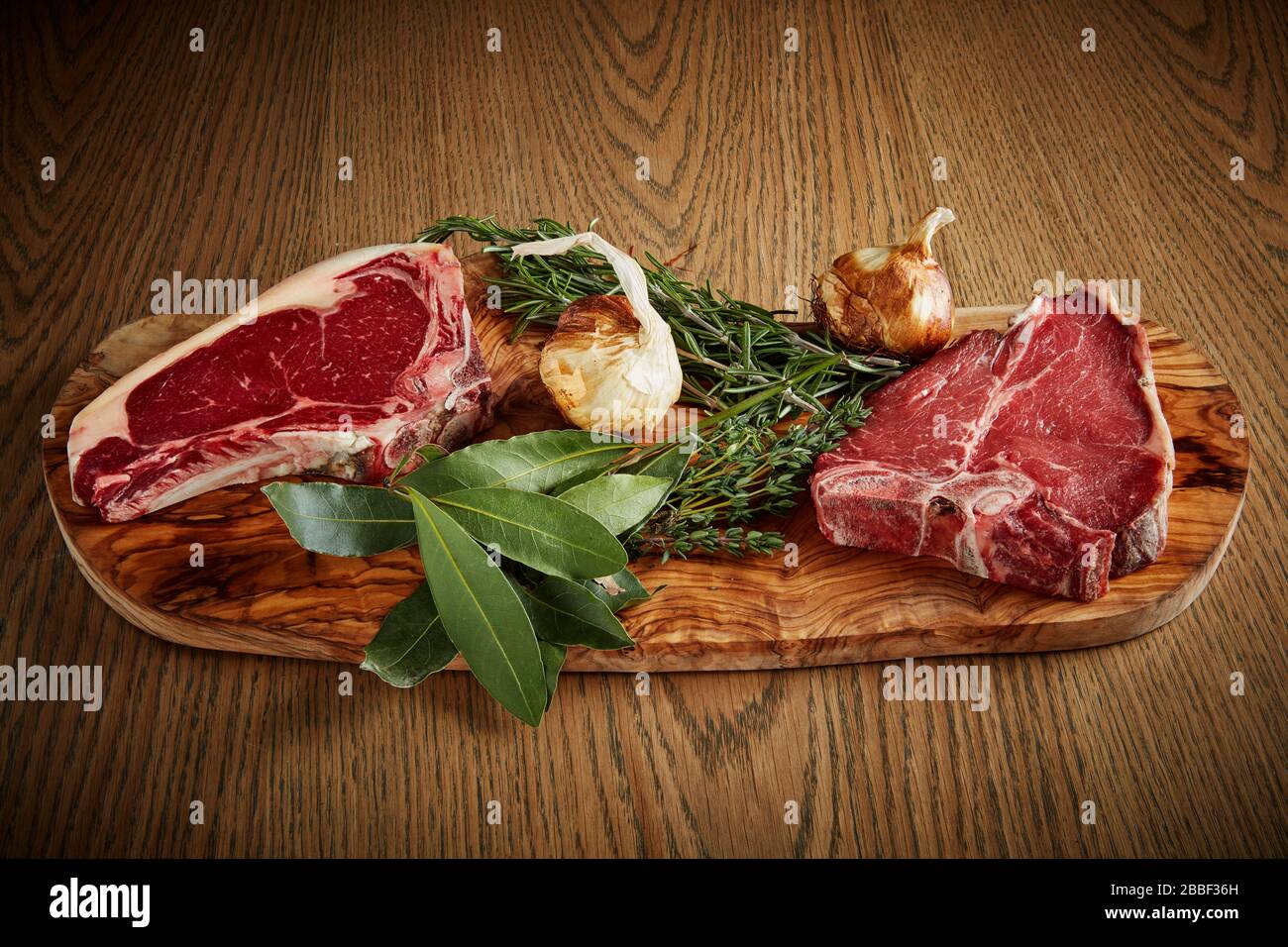 raw steak wood board rosemary bay leaf table top garlic Stock Photo