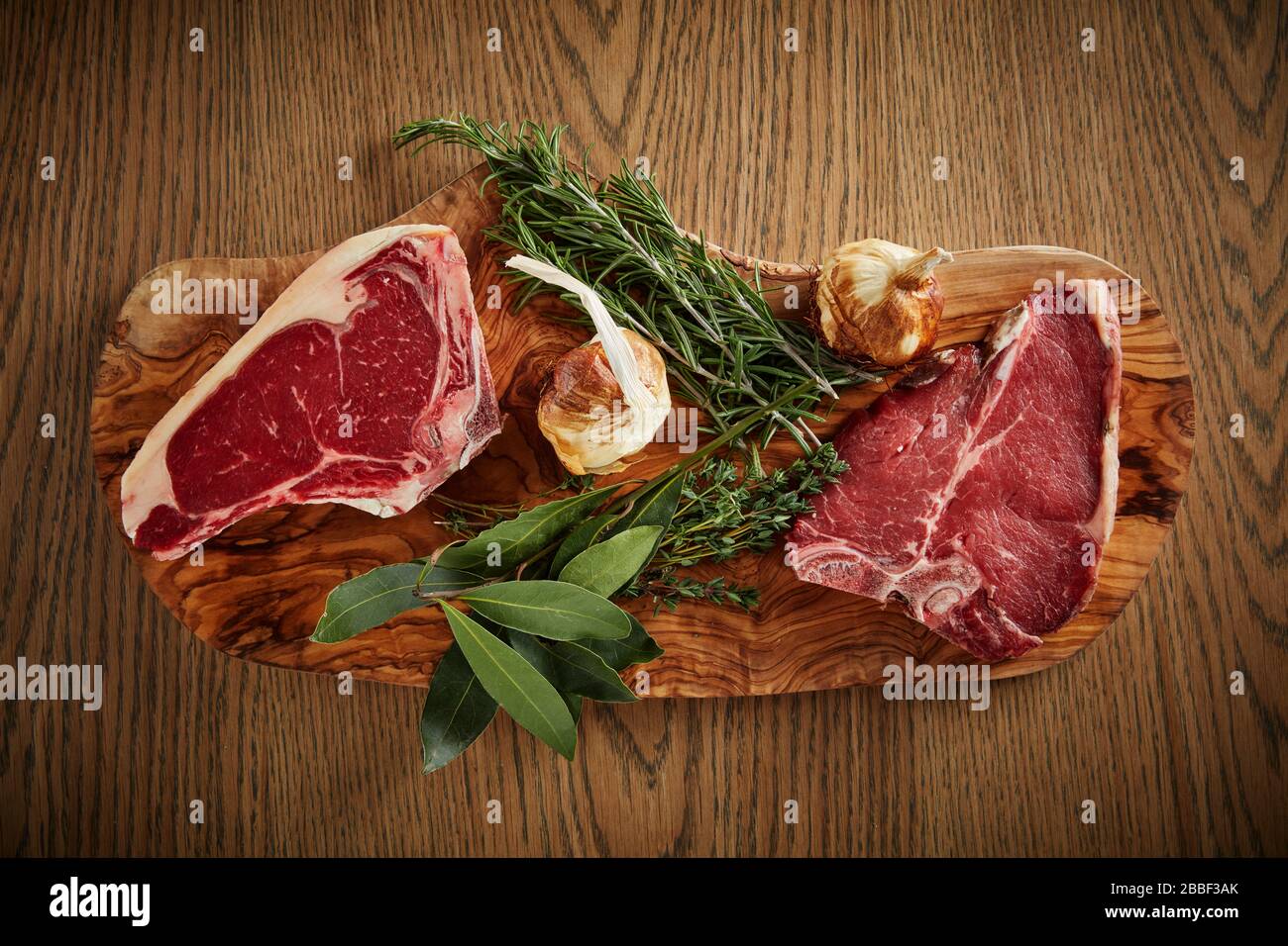 raw steak wood board rosemary bay leaf table top garlic Stock Photo