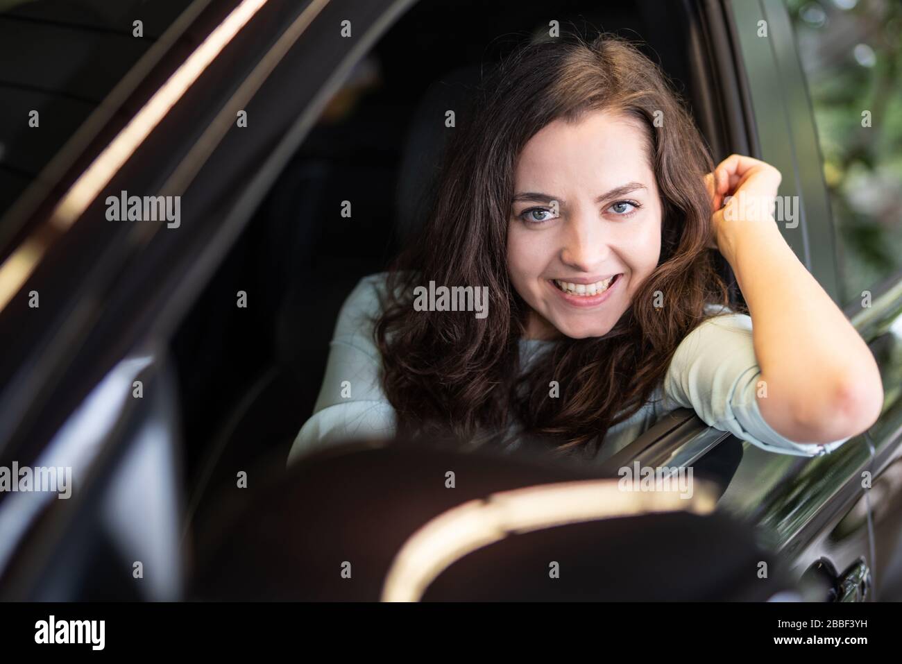 Cheerful laughing young woman sitting in a new car in a car dealership Stock Photo