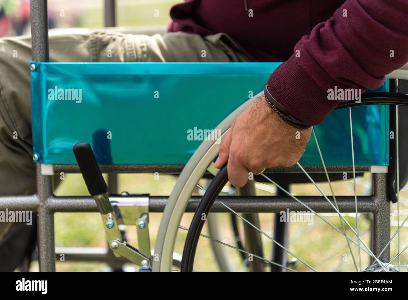 Hand of a paralyzed adult man in a wheelchair wearing a dark red sweatshirt in a park Stock Photo