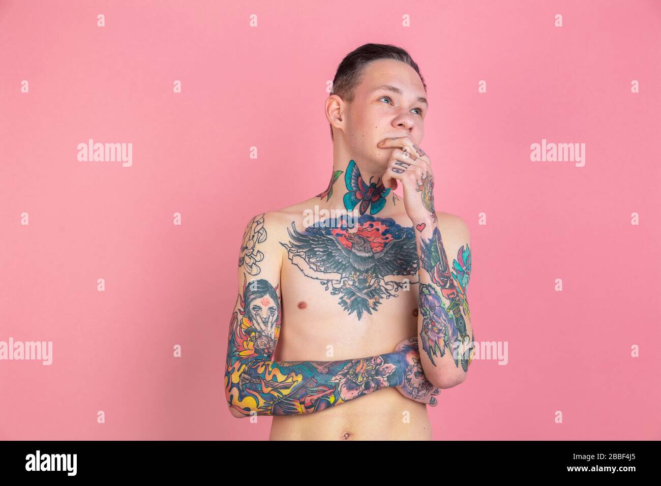 Thinking. Portrait of young man with freaky appearance on pink background. Unusual look with huge tattooes. Doing daily routine. Human emotions, facial expression, sales, ad concept. Youth culture. Stock Photo