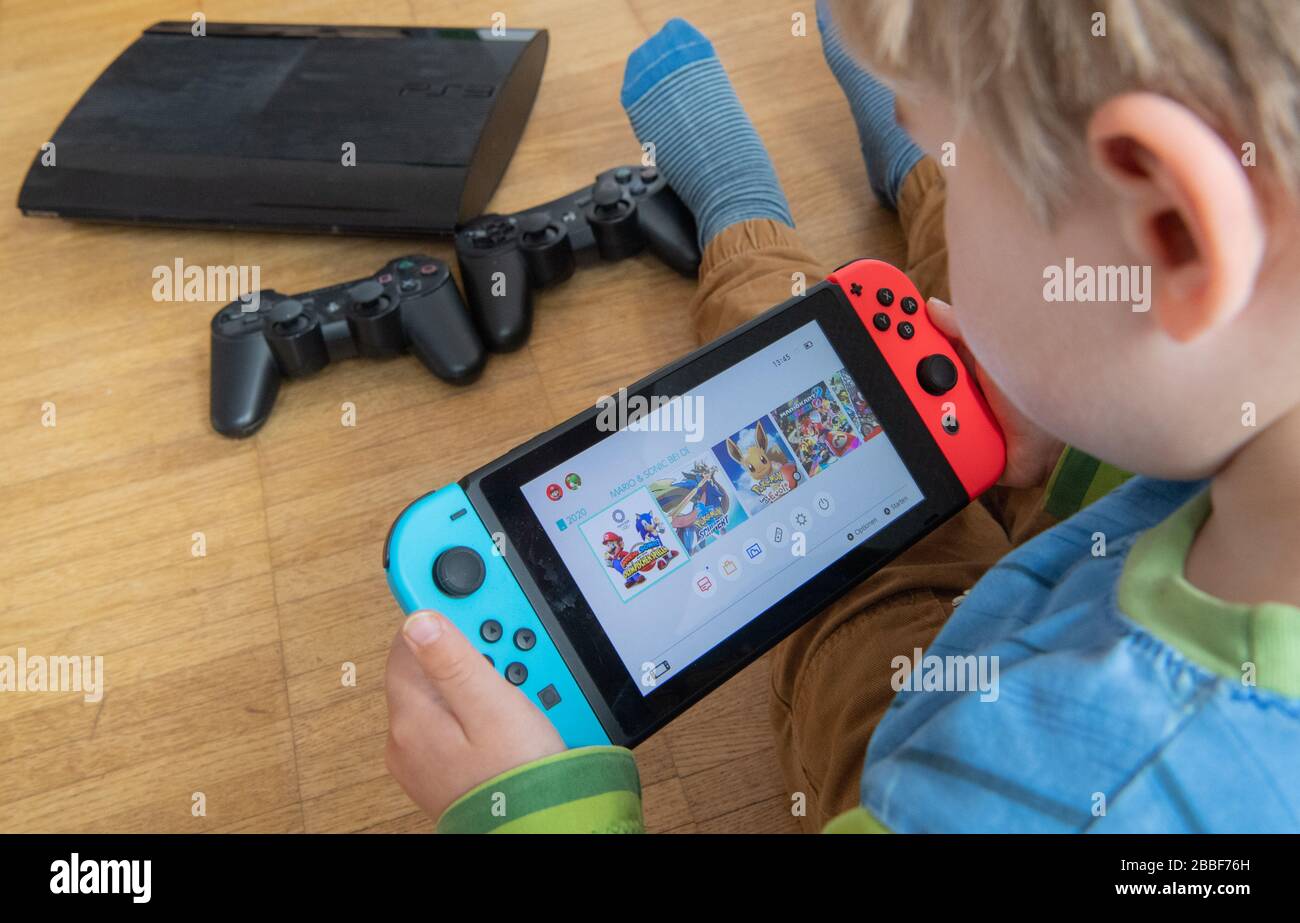 31 March 2020, Lower Saxony, Hanover: ILLUSTRATION - A child is playing with a Nintendo Switch game console while a Sony Playstation 3 with two controllers is seen in the background (scene posed) Photo: Julian Stratenschulte/dpa Stock Photo