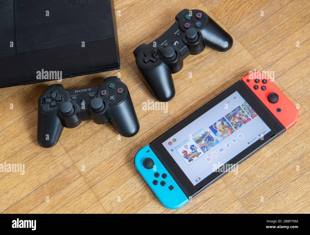 31 March 2020, Lower Saxony, Hanover: ILLUSTRATION - A Nintendo Switch type game console (front) and a Sony Playstation 3 with two controllers are lying on a parquet floor (posed scene) Because of the contact restrictions in the Corona crisis, criminologist Christian Pfeiffer sees a significantly increased risk of video and computer game addiction among children and young people. Photo: Julian Stratenschulte/dpa Stock Photo