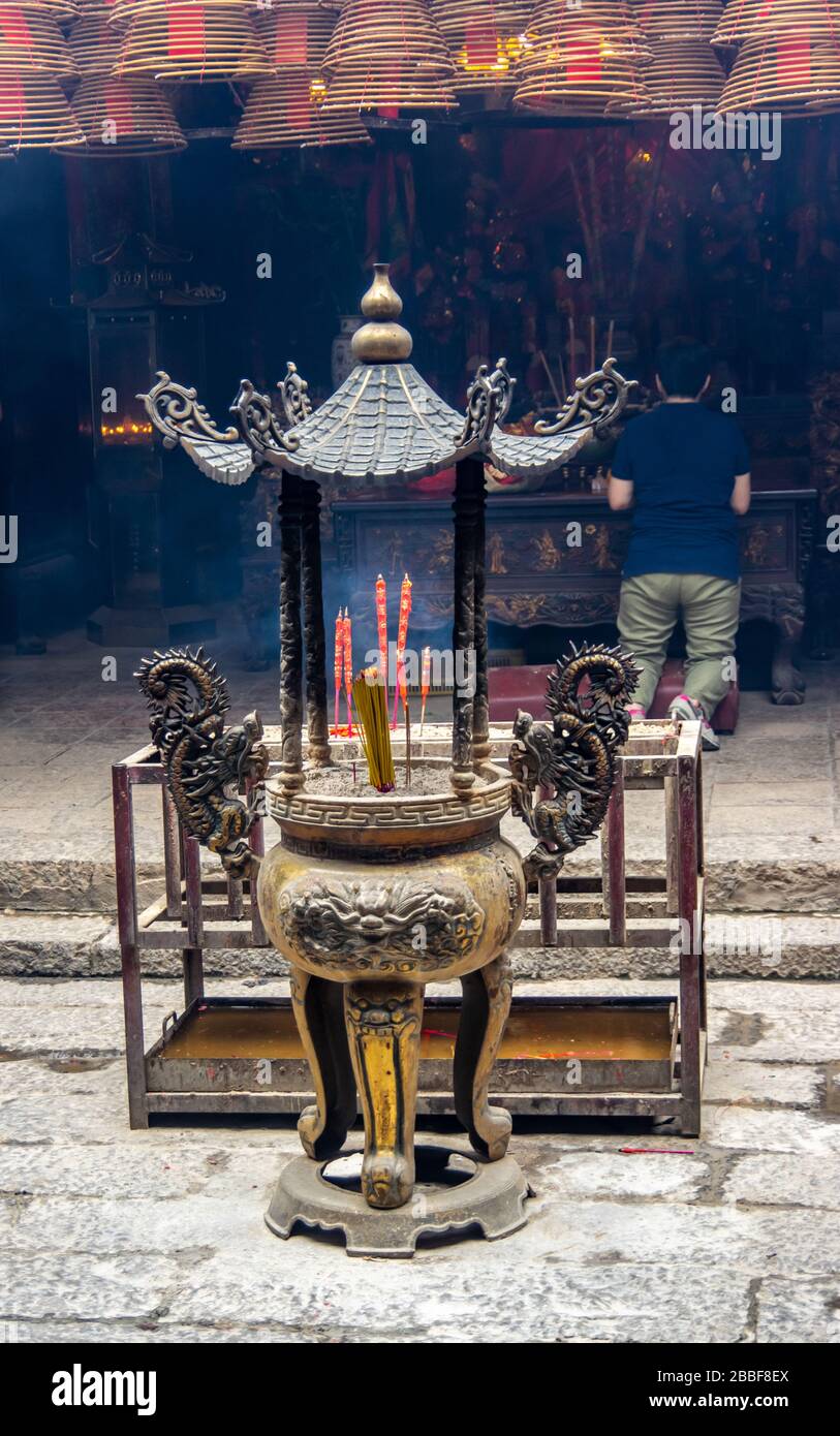 Incense burning at a Buddhist shrine with a woman praying in the