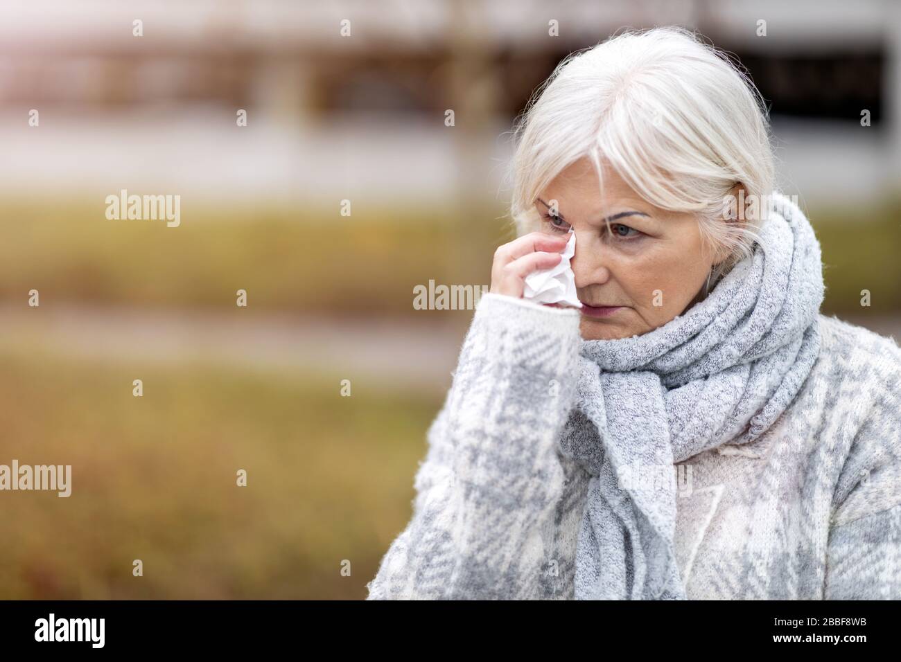 Unhappy senior woman wipes her eyes with a tissue Stock Photo