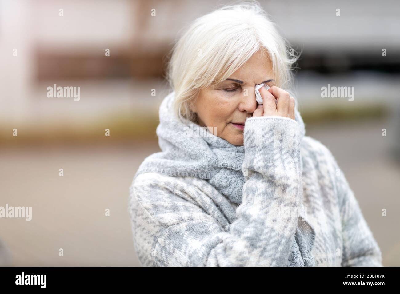 Unhappy senior woman wipes her eyes with a tissue Stock Photo