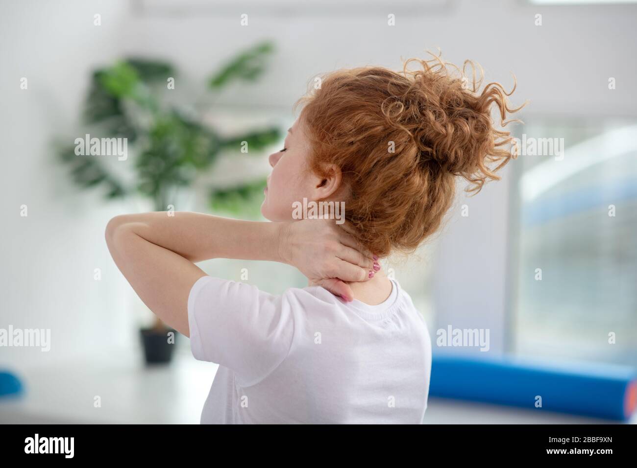 Red-haired female patient massaging her painful neck Stock Photo - Alamy