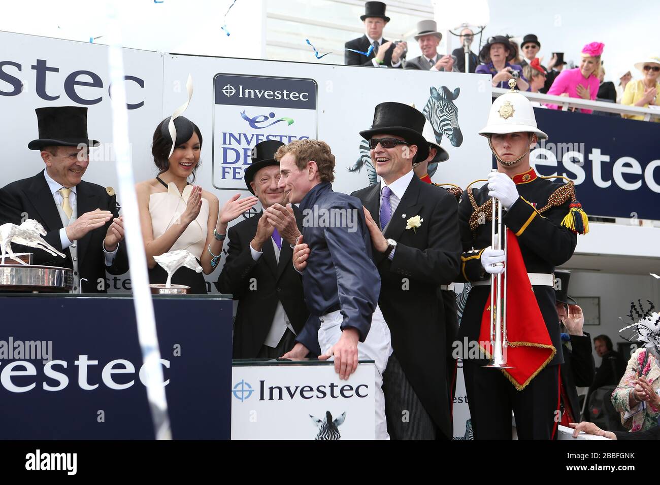 Ruler of the World jockey Ryan Moore is congratulated by co owner Michael Tabor (left) Actress and Investec Derby Ambassador Gemma Chan (second left) and trainer Aidan O'Brien (right) after victory in the Investec Derby Stock Photo