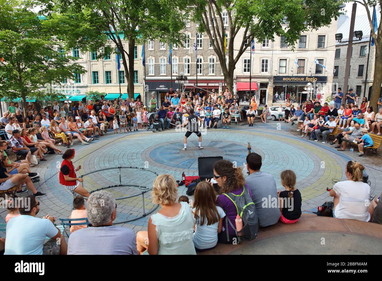 Crowd of people watching a couple take turns performing acrobatic tricks at Place de l'Hotel de Ville in Old Quebec City, Province of Quebec, Canada Stock Photo