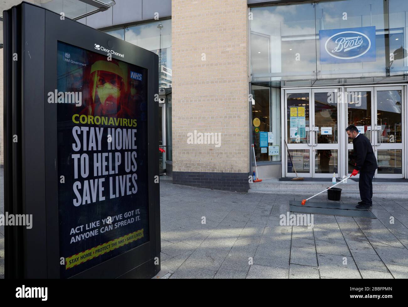 Birmingham, West Midlands, UK. 31st March 2020. A worker cleans the steps  of a Boots chemist in front of a NHS advert in Birmingham city centre  during the Coronavirus pandemic lockdown. Credit