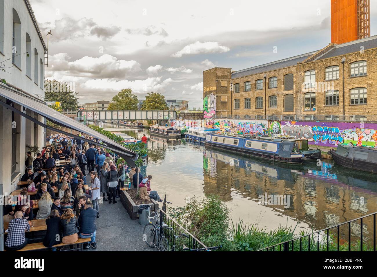 Groups of young hipsters socialise on a riverside bar and restaurant terrace on the bank of the river lea in Hackney Wick, East London, uk Stock Photo