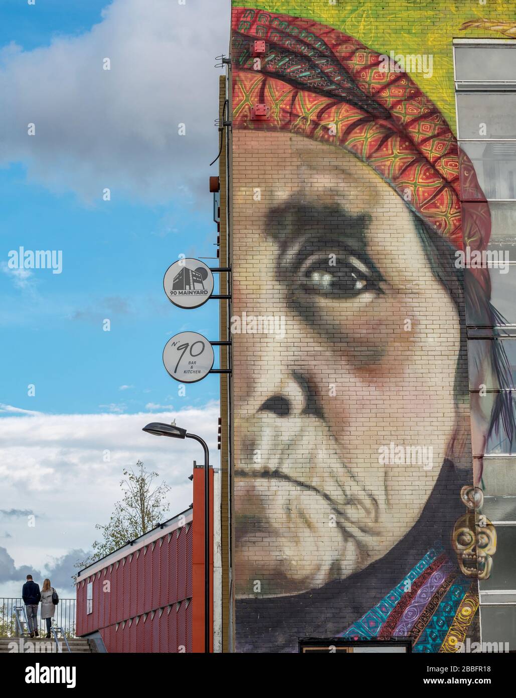 A couple walking on a bridge over the River Lea in Hackney Wick in East London. A commissioned graffiti artists mural makes up the foreground Stock Photo