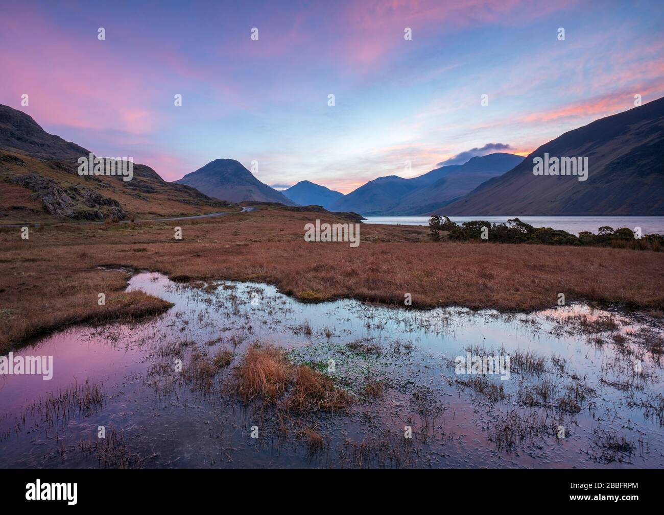 A beautiful pastel sunrise provides a backdrop for the dramatic high fells of the English Lake District at the top of Wast Water, Wasdale. Stock Photo