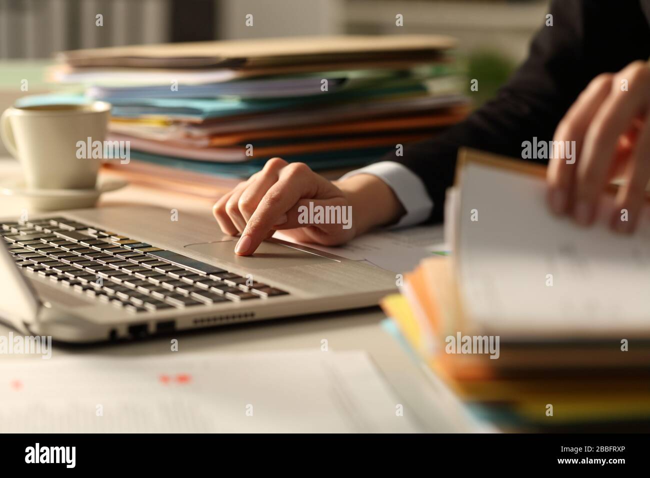 Close up of executive hands working hard late hours using laptop in the night at office checking a pile of documents Stock Photo