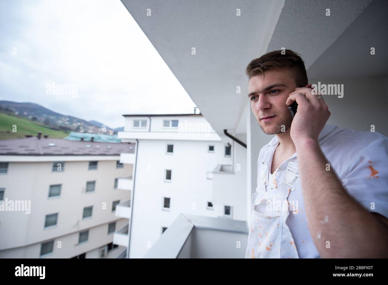 Painter making telephone call while standing on balcony during break from work Decorator Using Mobile Phone Standing Outside Stock Photo
