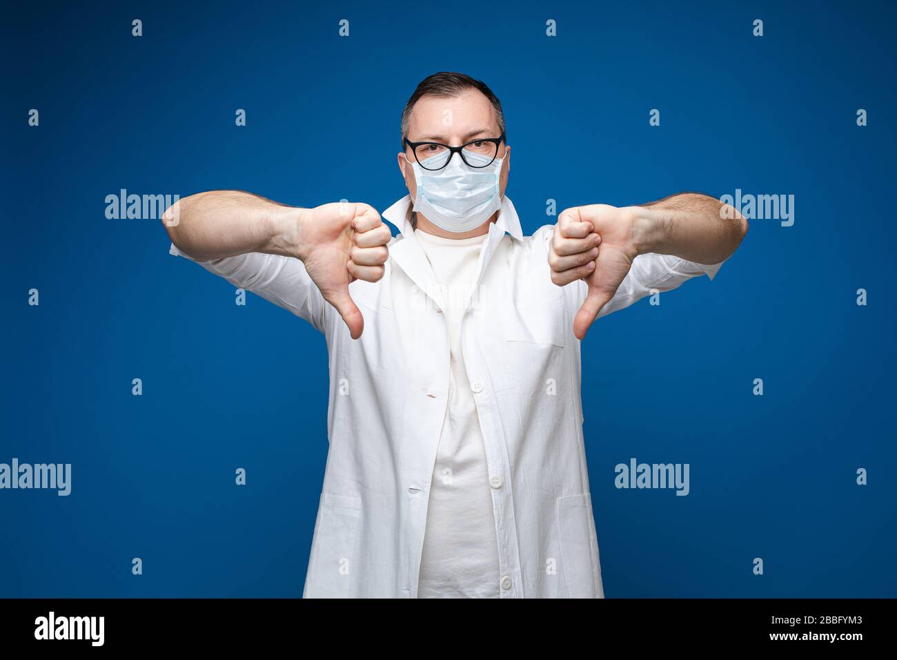A strong man with glasses, white medical gown and mask stands and shows ...