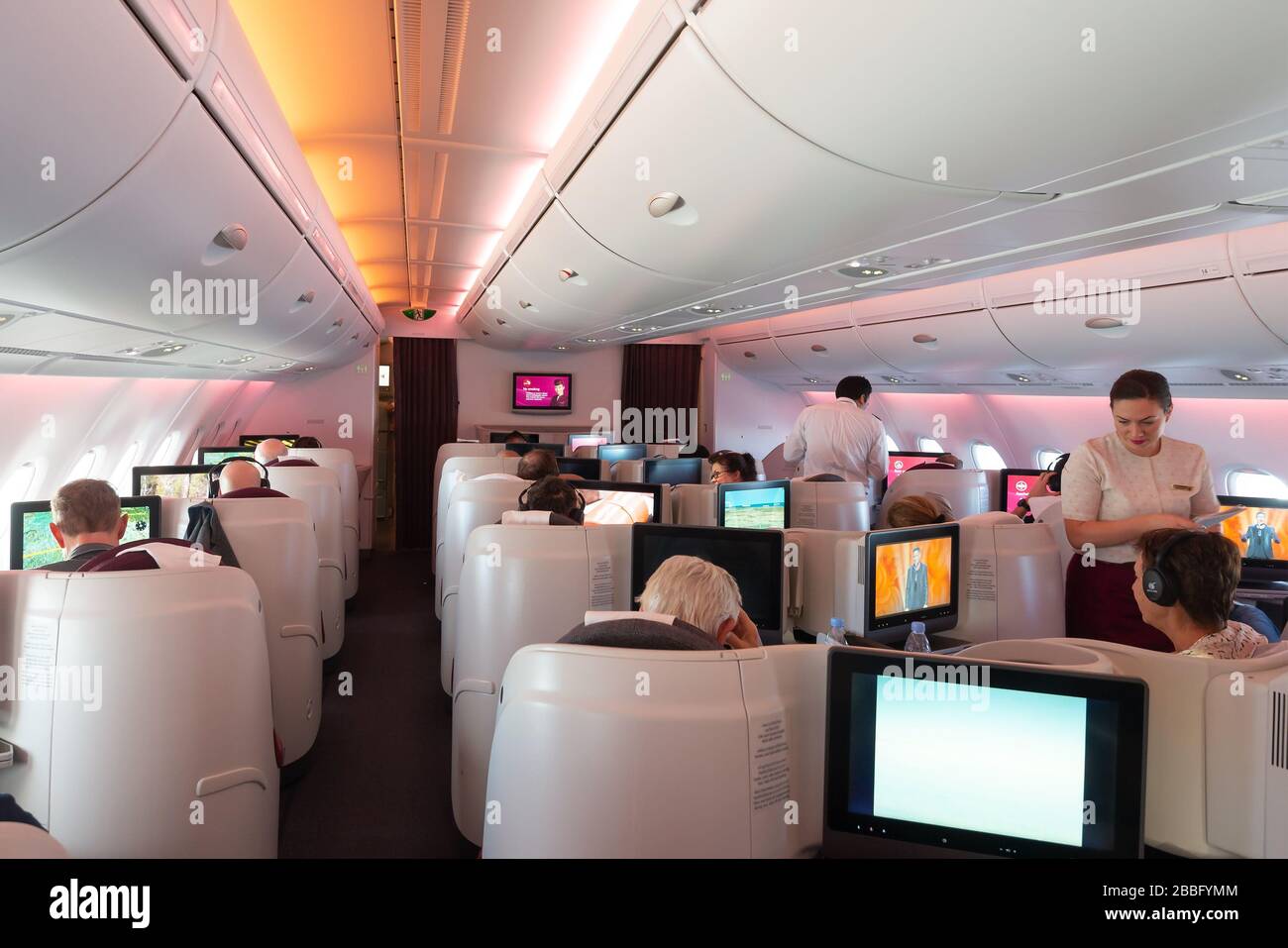 Qatar Airways Airbus A380 Business Class cabin with reverse herringbone seats. Skytrax five stars airline with hub in Doha. Qatari flight attendant. Stock Photo