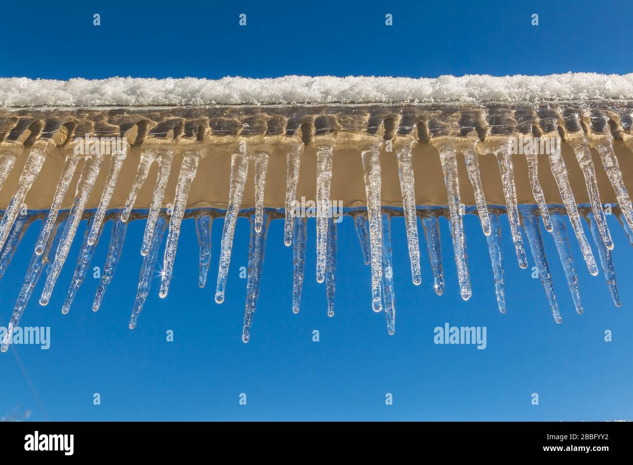 Close-up of tan painted wooden beam covered with snow, thick ice and icicles after ice storm in early spring, Laval, Quebec, Canada Stock Photo