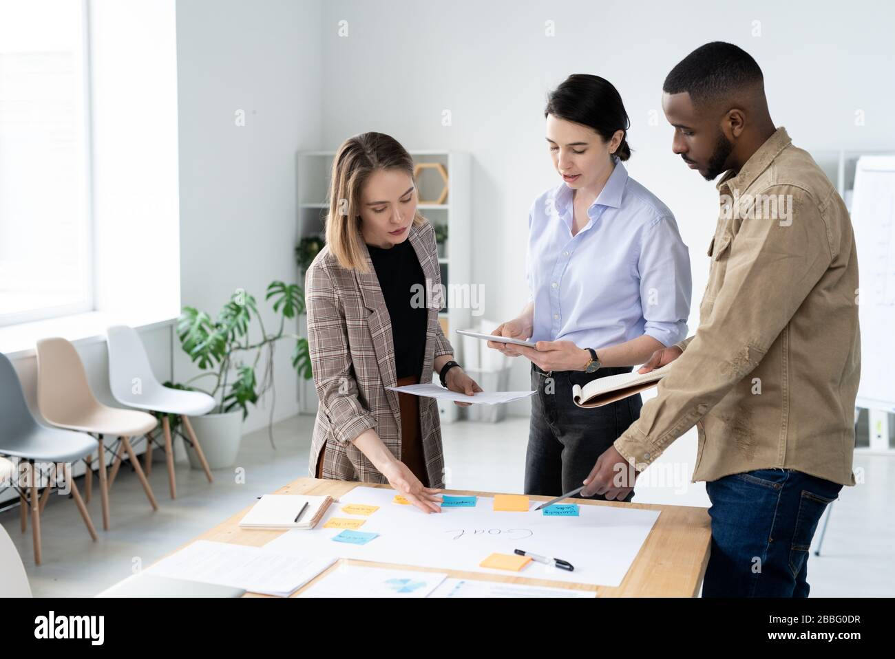 Busy young interracial colleagues discussing creative ideas for startup project while making task board Stock Photo