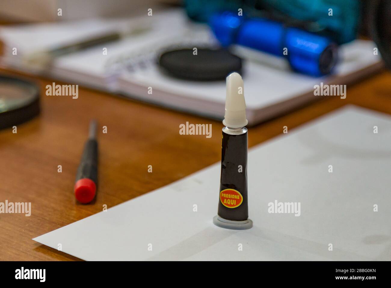 A black tube with a white cap with universal glue stands on a table with a screwdriver and other tools, prepared for equipment repair. Close up macro Stock Photo