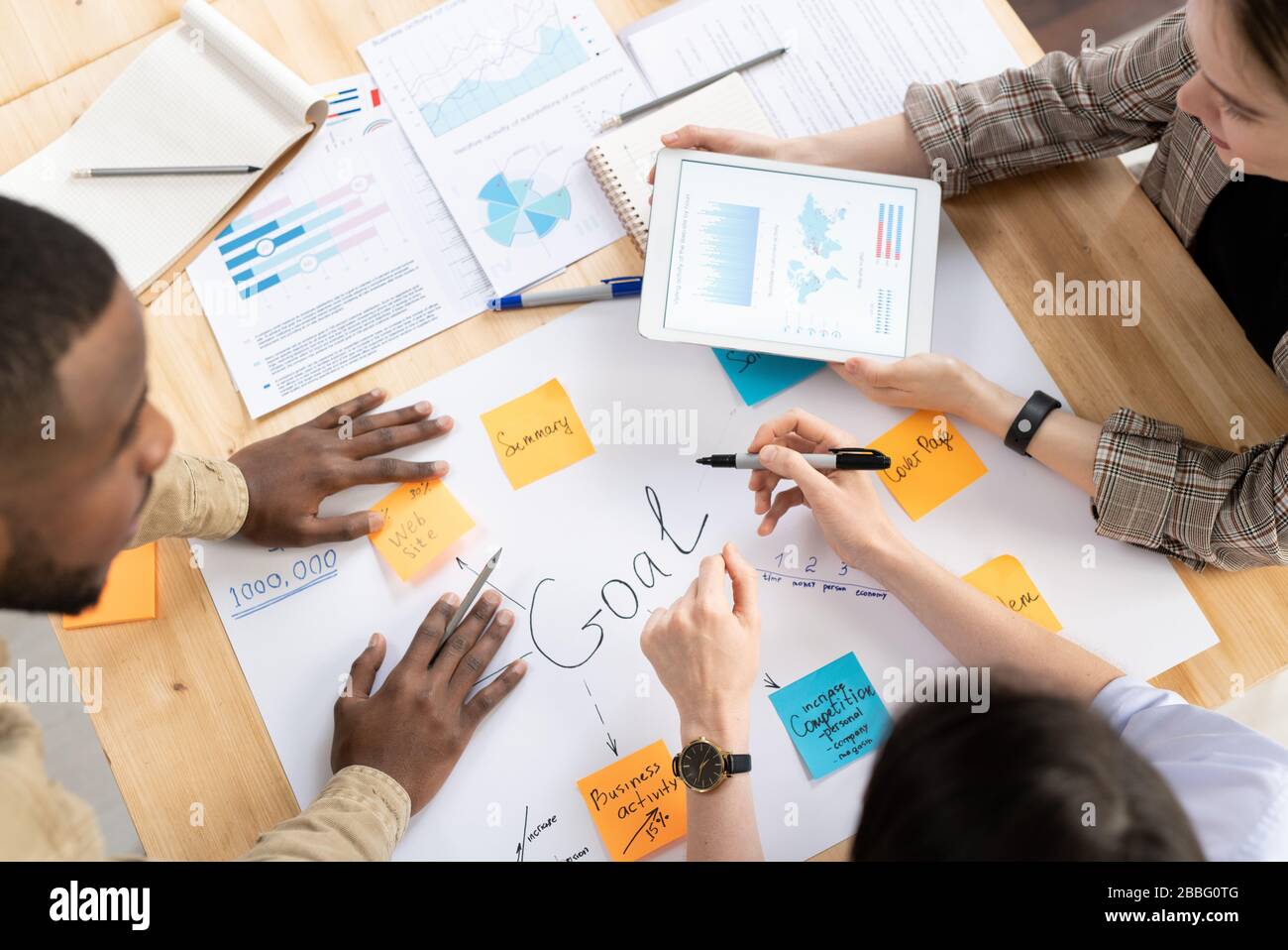 Above view of multi-ethnic colleagues standing around desk and working on business plan together at meeting Stock Photo