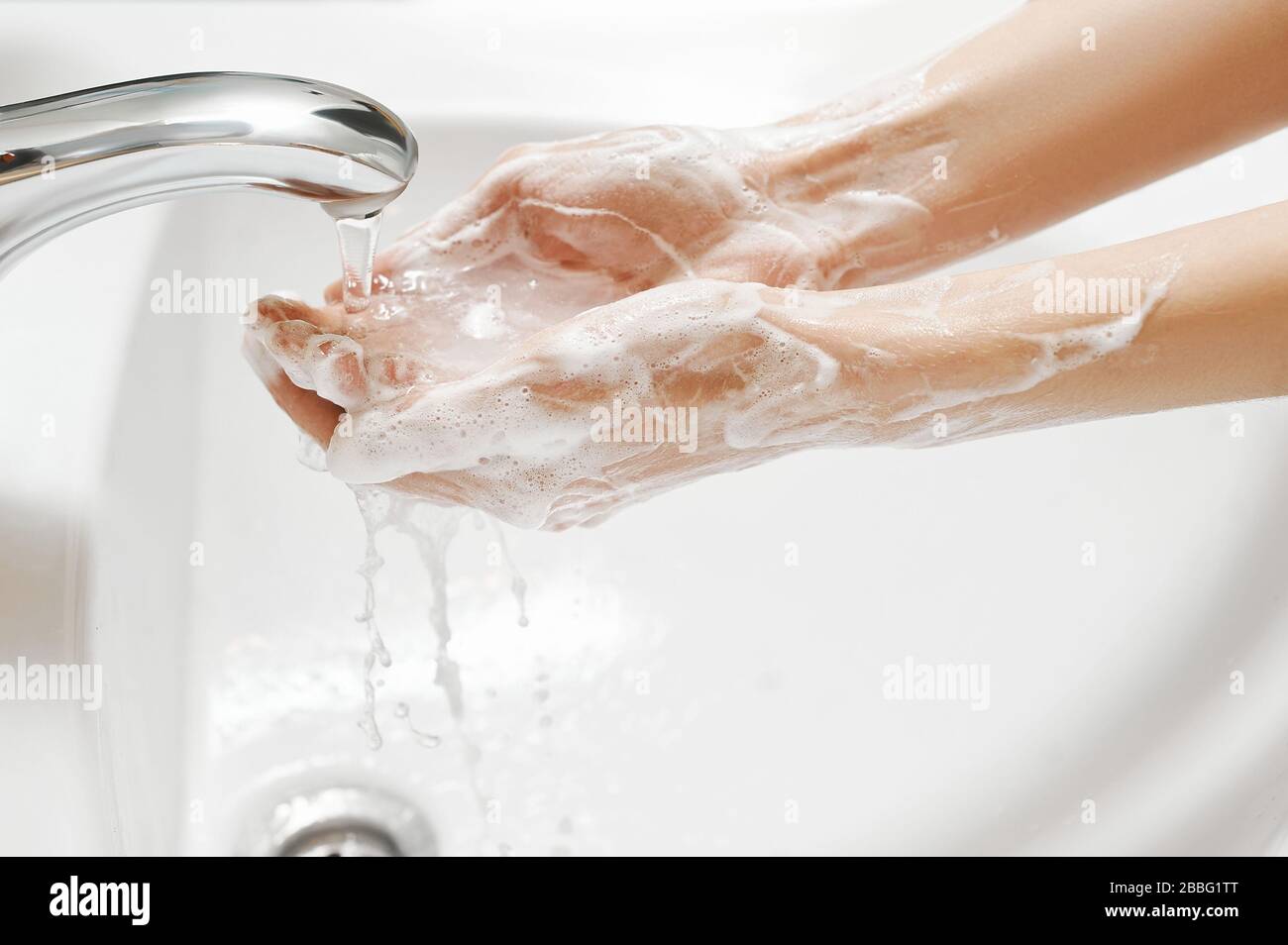 Hand Washing in white sink. Water flows from a faucet at soapy female hands. Covid-19 coronavirus protective measure. Stock Photo