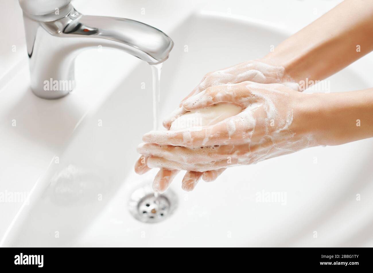 Hand Washing in white sink. Water flows from a faucet at soapy female hands. Covid-19 coronavirus protective measure. Stock Photo