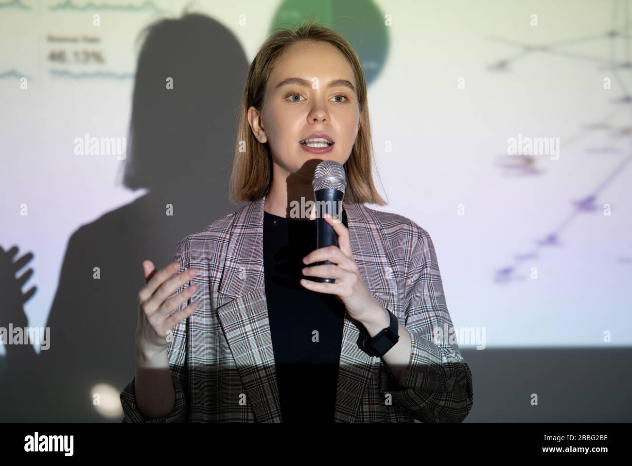 Confident young businesswoman speaking about her success into microphone at entrepreneurship conference Stock Photo