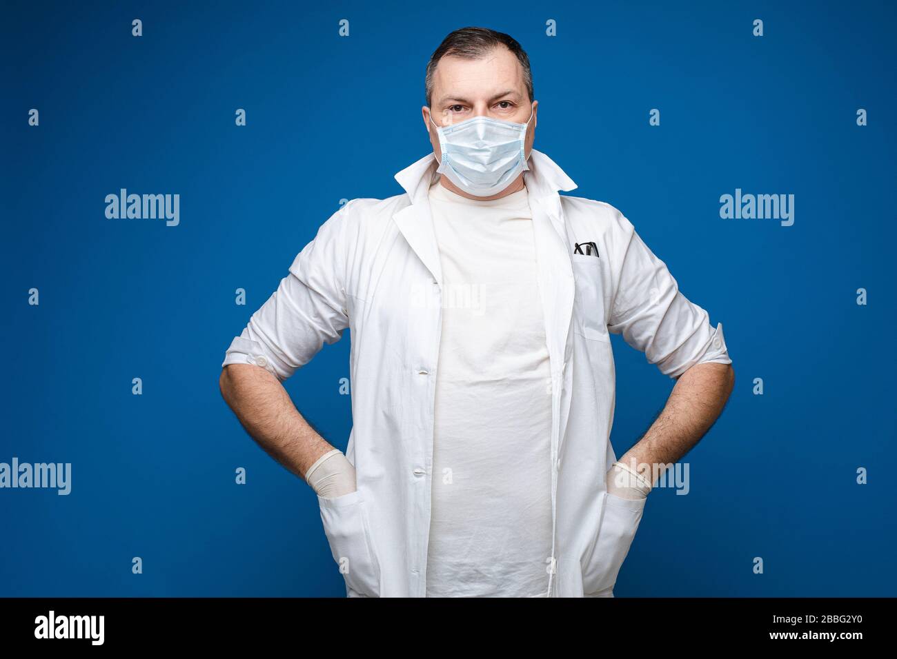 A strong man with glasses, white medical gown and mask stands with ...