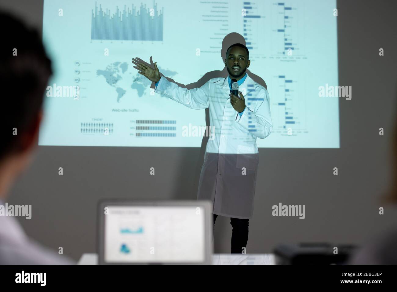Confident young Afro-American medical scientist in lab coat showing statistics on spread of coronavirus while presenting solution to stop it Stock Photo