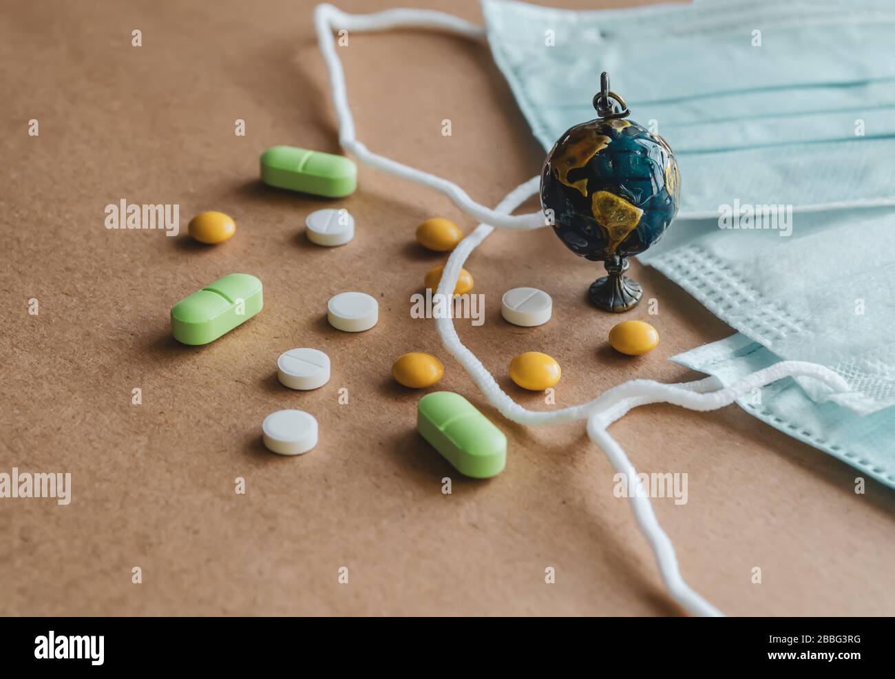 Blue medical disposable protective mask, small globe and a scattering of pills on a brown background. Coronavirus concept Stock Photo