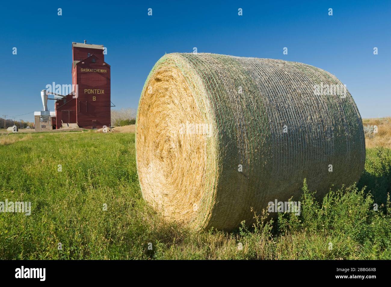 round alfalfa bales and grain elevator, Ponteix, Saskatchewan, Canada Stock Photo