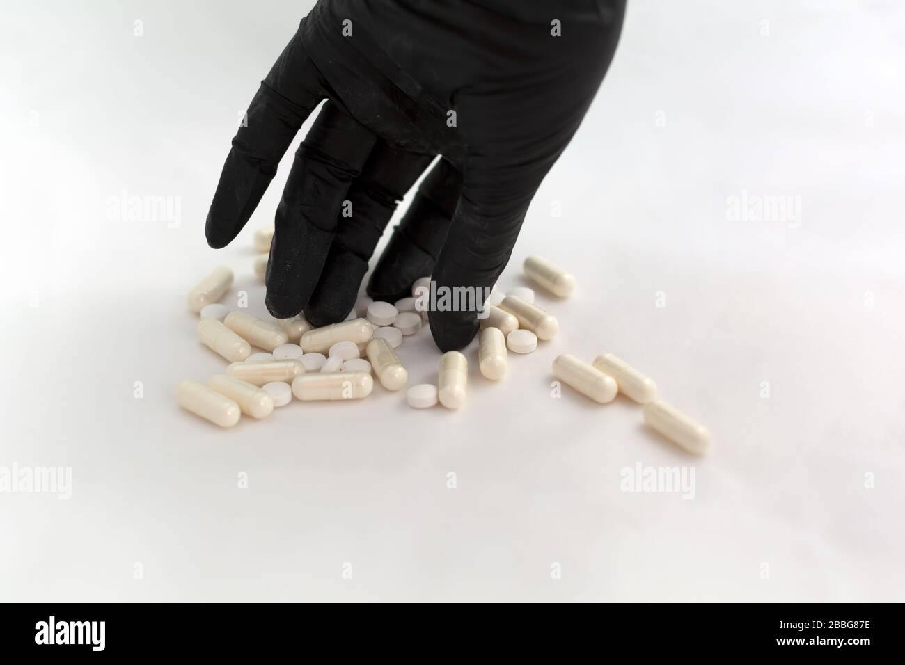 Hand in black latex glove taking pill from a bunch of drugs Stock Photo