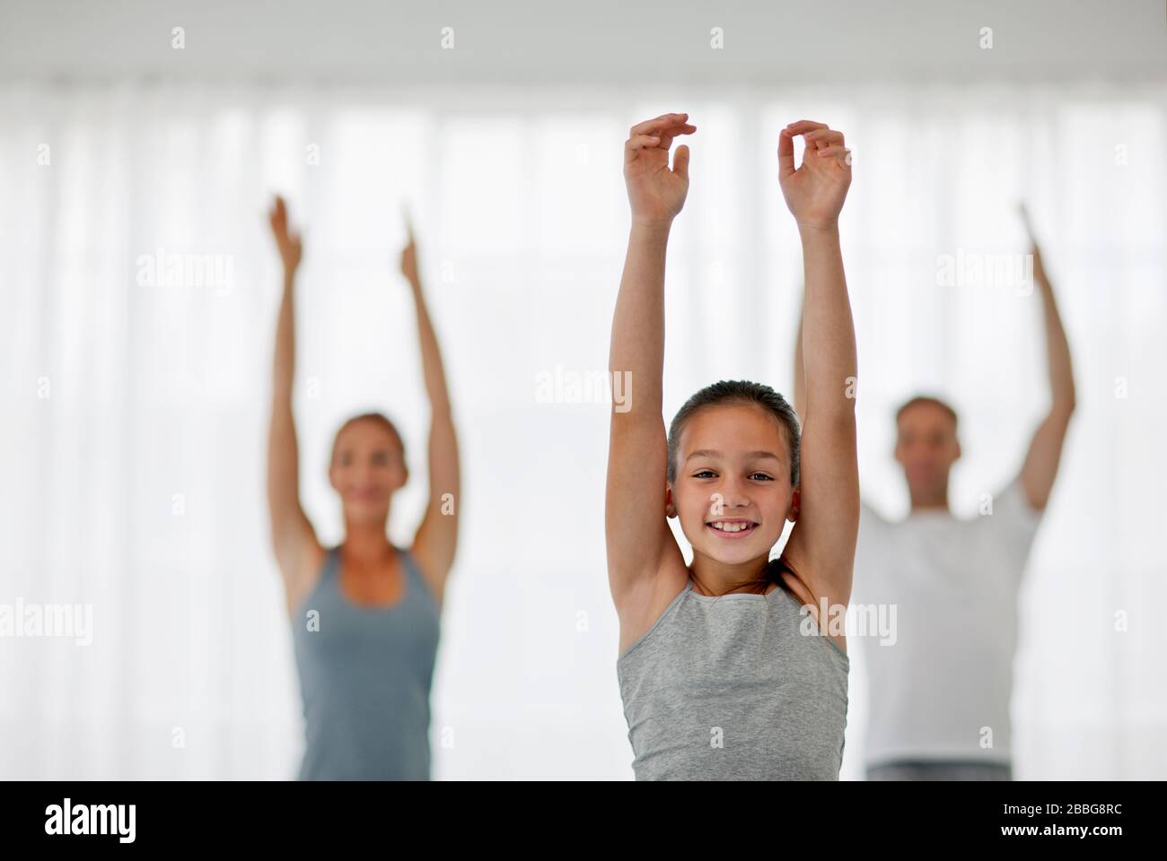 Portrait of a young girl stretching while doing yoga with two adults in the background Stock Photo
