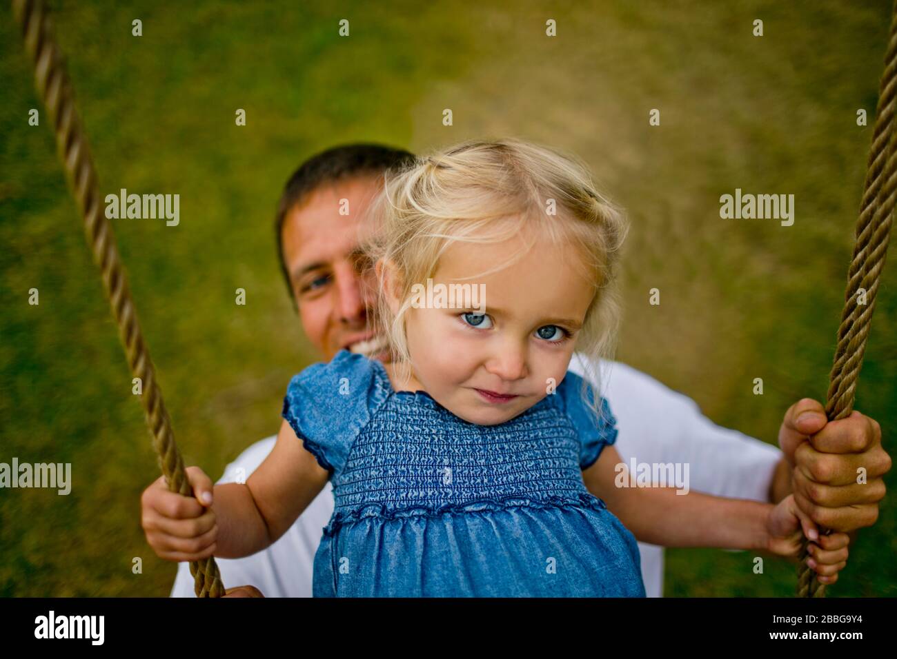 Portrait of a young girl playing on a rope swing with her father Stock Photo