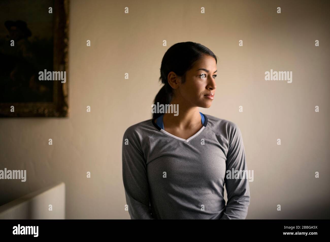 Portrait of a young woman looking thoughtfully into the distance while standing indoors Stock Photo