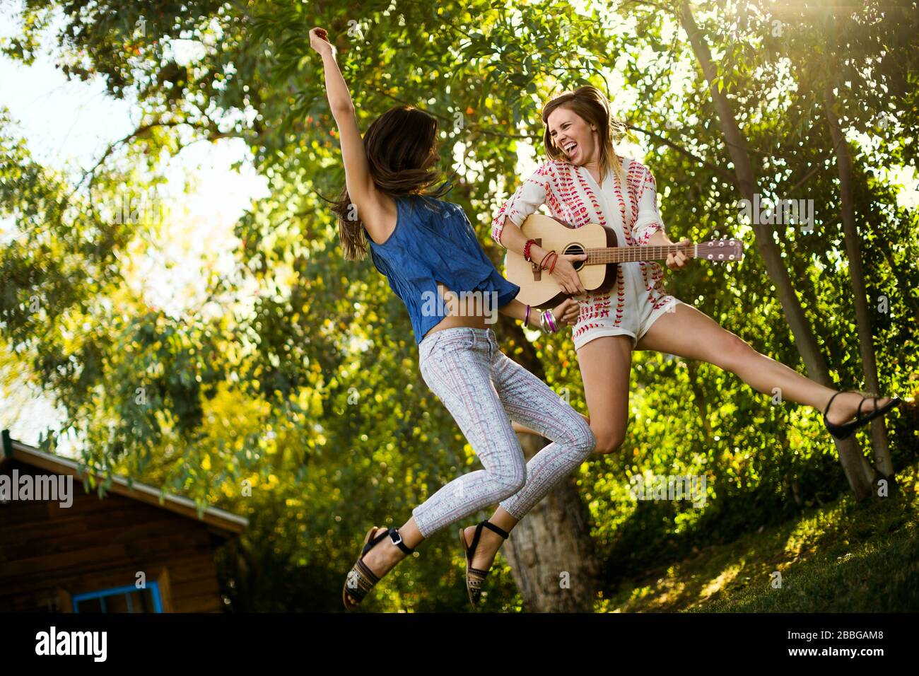 Two happy mid adult women jumping up in the air holding a guitar Stock Photo