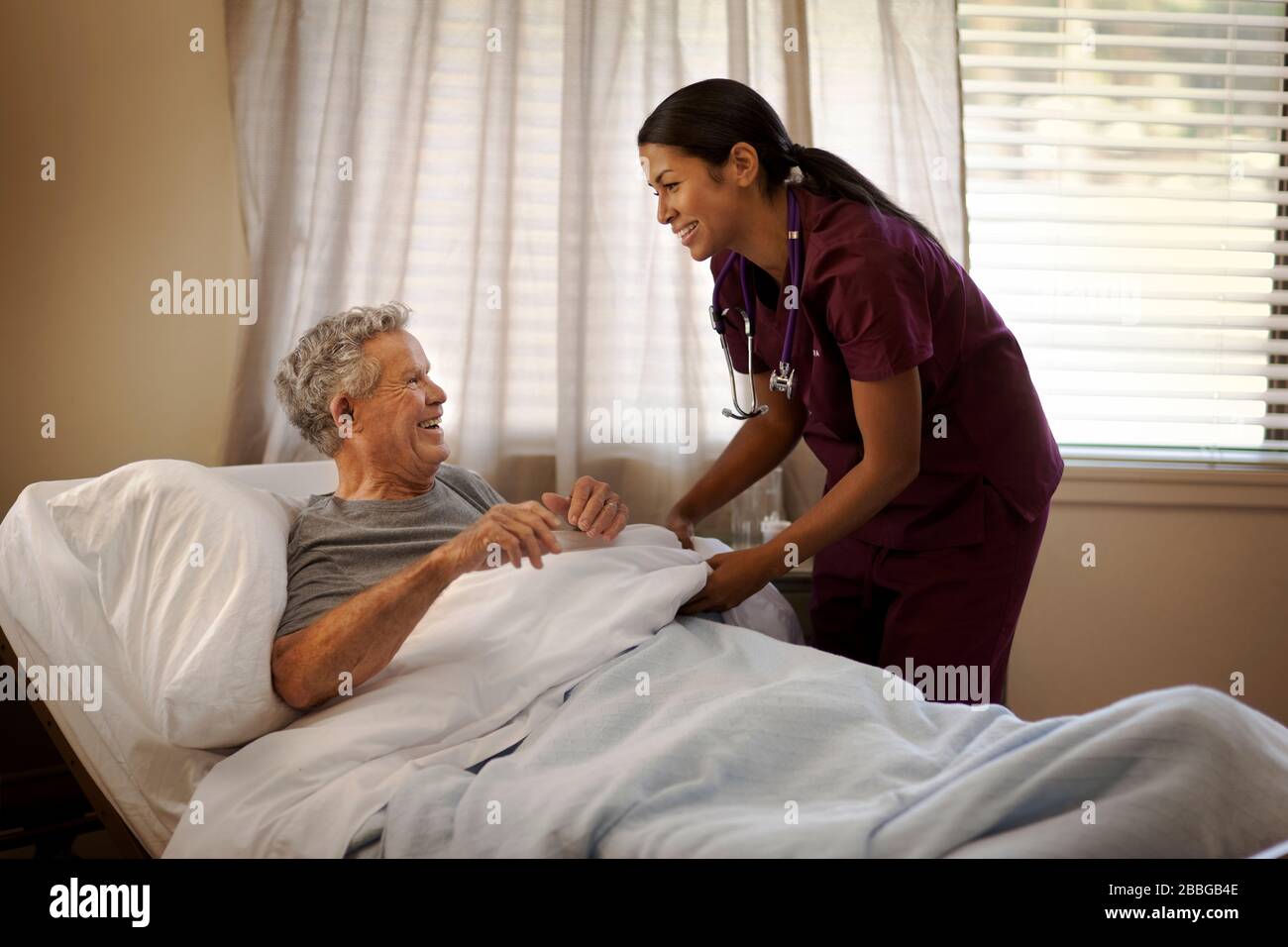 Smiling young nurse tucking in a senior man in a hospital bed Stock Photo
