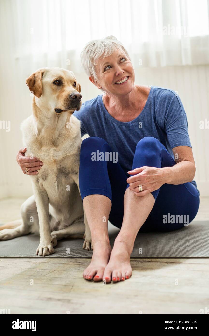 Smiling mature woman sitting on a yoga mat with her dog Stock Photo